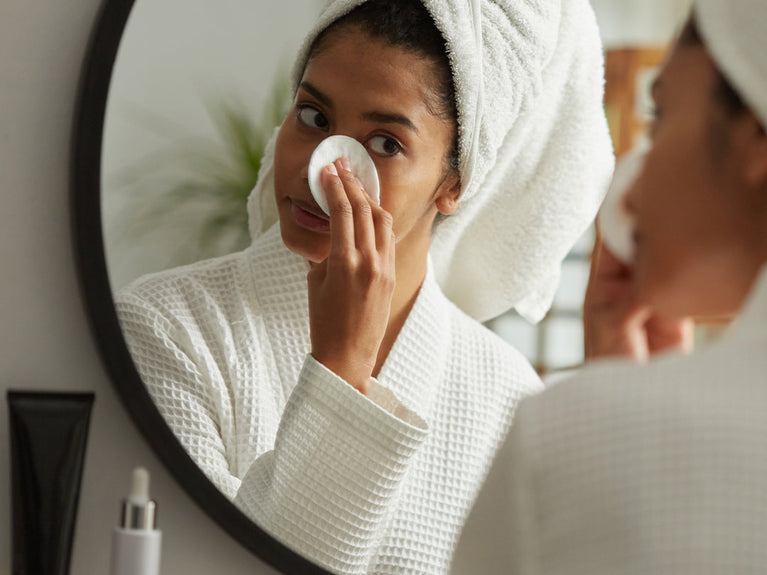 Image of women looking in the mirror and using a cotton pad on her undereye